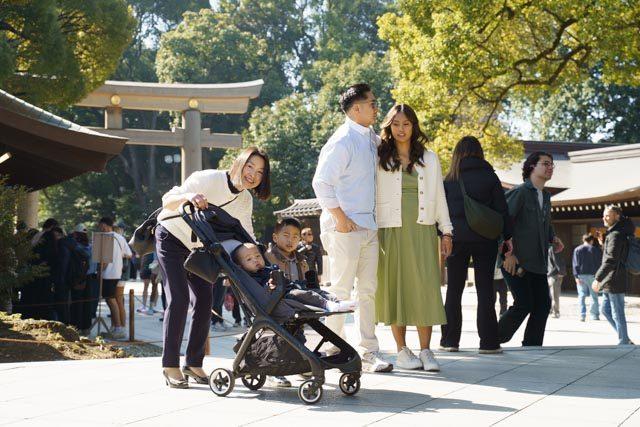A Travel Nanny walking a shrine path with two children in a stroller while their parents walk alongside